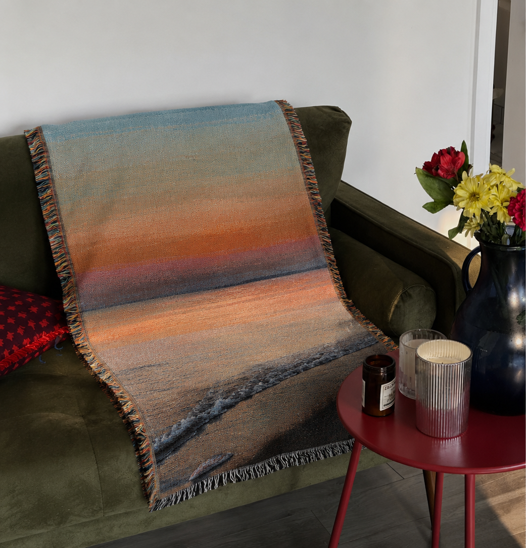 Lakeside Sunset woven throw draped over a deep green sofa beside flowers and candles