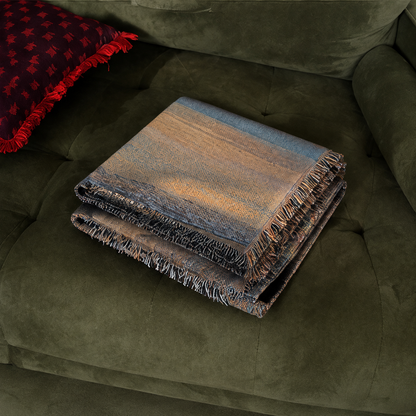 Lakeside Sunset woven throw folded on a deep green sofa, close-up view